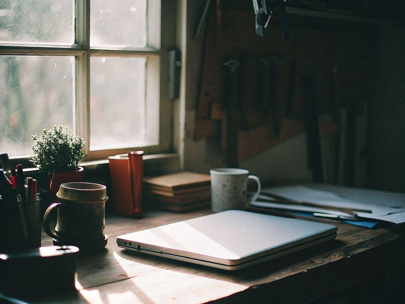 Rincón de escritorio de un taller con un portátil cerrado, una taza y una planta